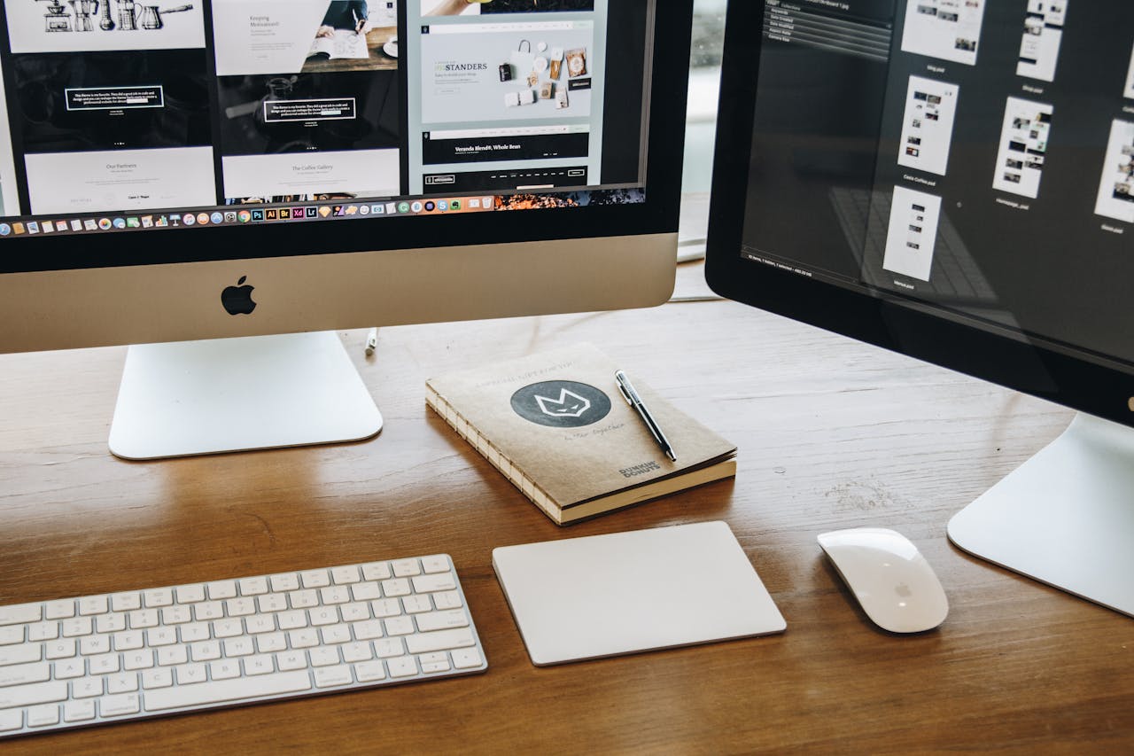 A minimalist desk setup featuring dual monitors, keyboard, mouse, and notebook for productivity.